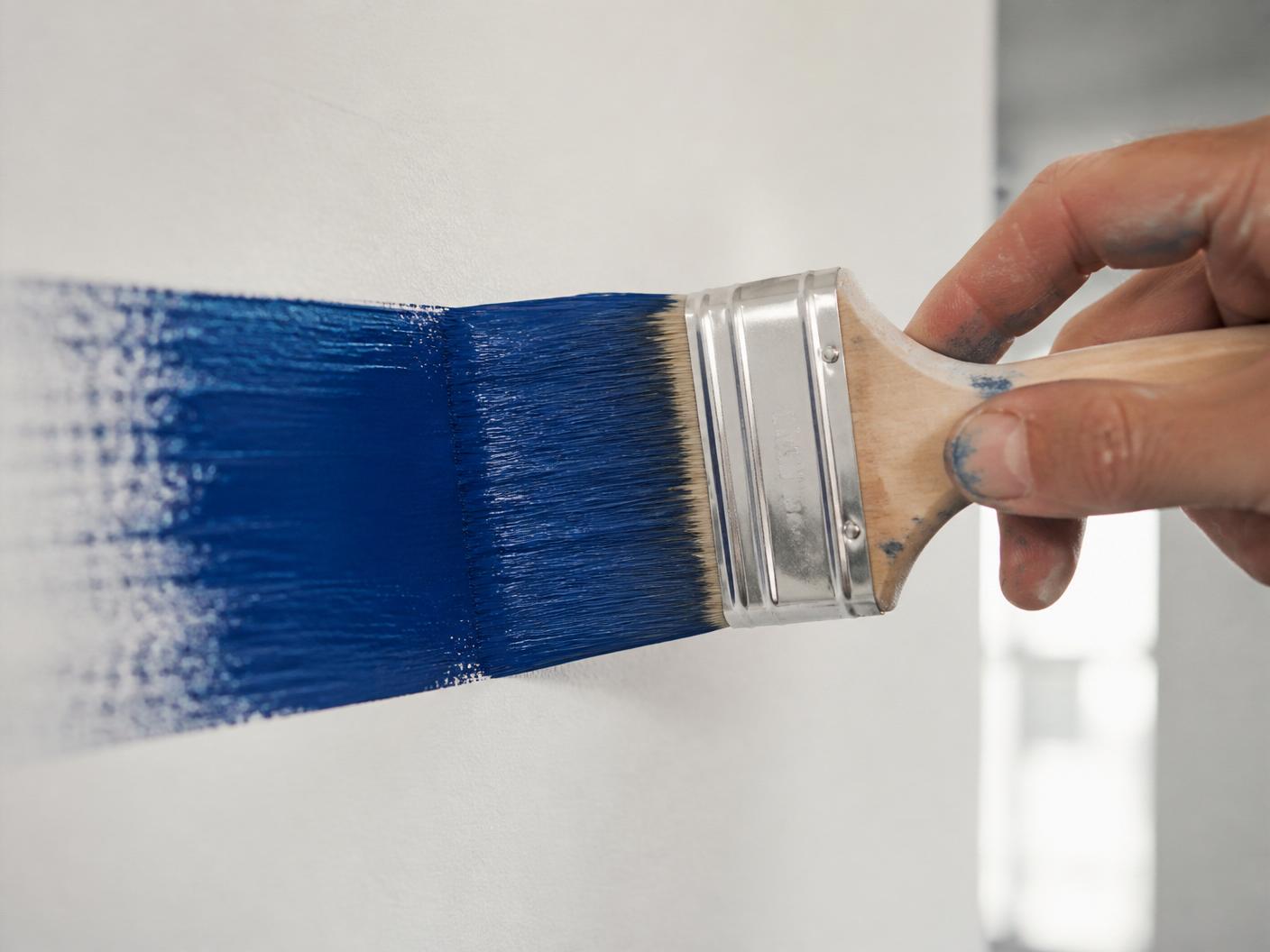 Detalle de brocha aplicando pintura cobalto en una pared blanca — proceso profesional de pintura